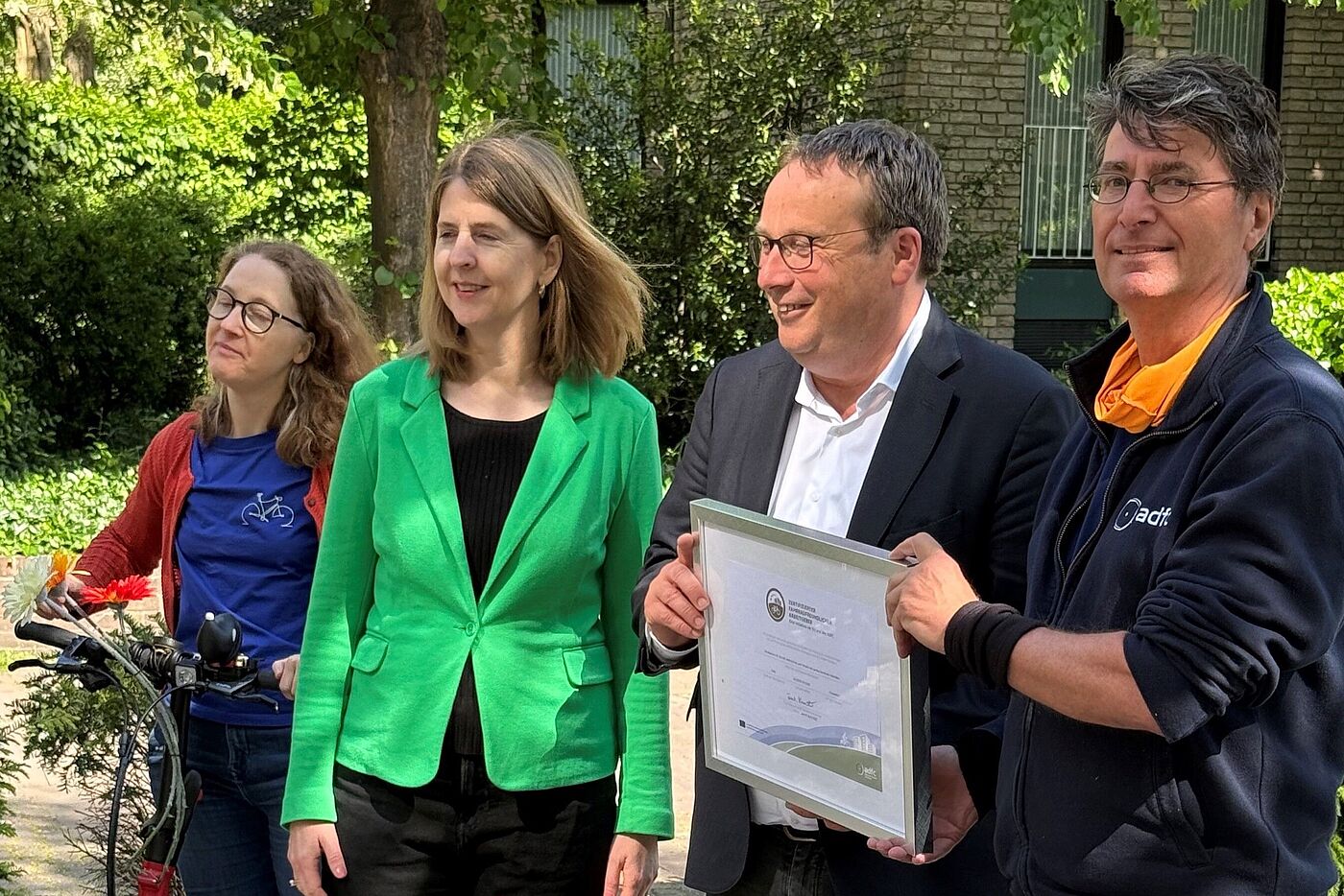 Minister Krischer (2. v. r.) hält das Zertifikat für das Ministerium für Umwelt, Natur und Verkehr (MUNV) des Landes Nordrhein-Westfalen in der Hand. Die Übergabe für die Re-Zertifizierung erfolgte am 6. Mai 2025. v. l. n. r. Susanne Niemann (Landesvorsitzende ADFC NRW), Dr. Sandra Terporten (Referatsleiterin „Rad- und Fußverkehr, Verkehrssicherheit“, MUNV), Oliver Krischer (Minister MUNV), Dr. Andreas K. Bittner (Auditor, ADFC NRW)